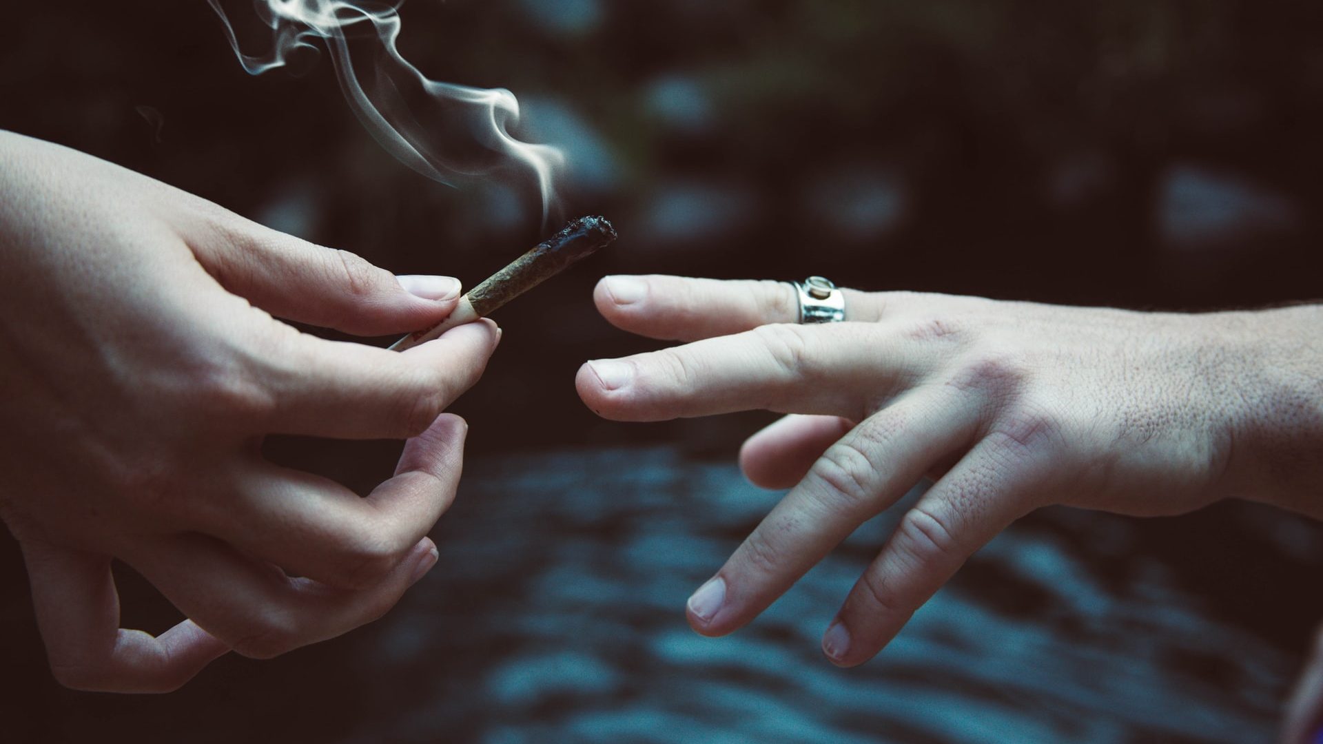 two hands passing a cannabis joint